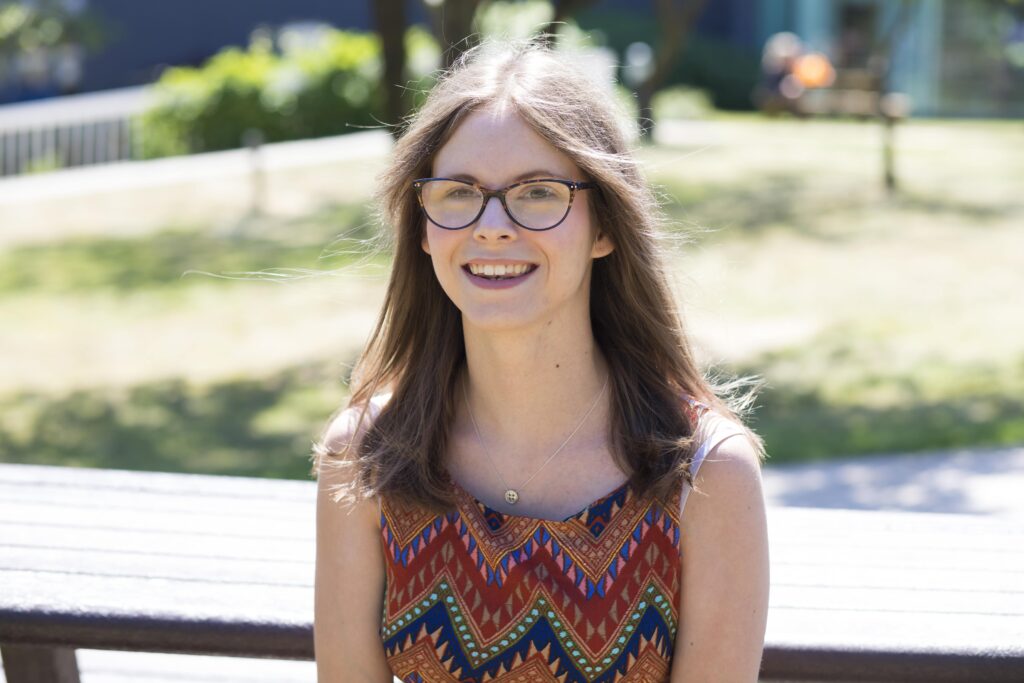 Chloe Tear, a white woman with brown hair and black glasses facing and smiling to the camera