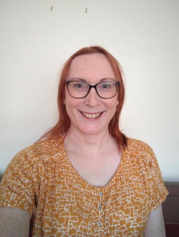 Sarah Ward, a white woman with red hair wearing black glasses smiling to the camera