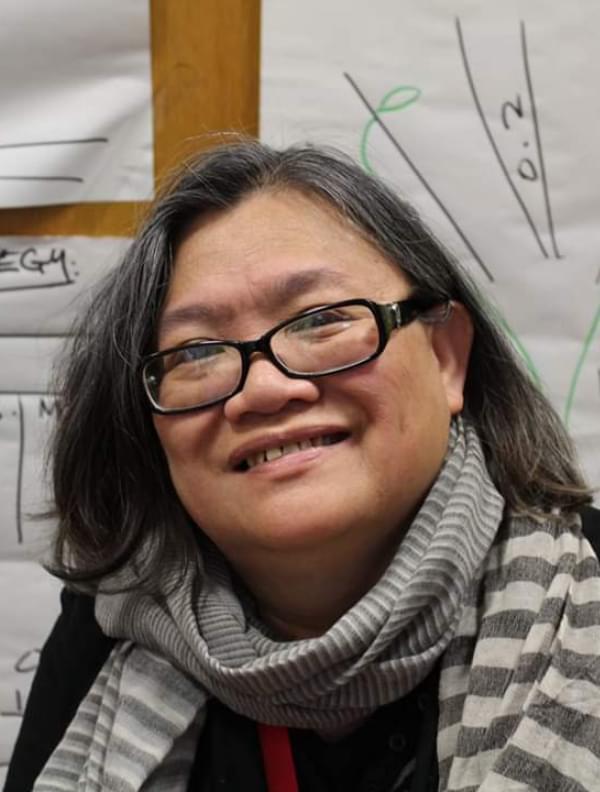 Eleanor Lisney, an Asian woman with black hair wearing black glasses and smiling to the camera