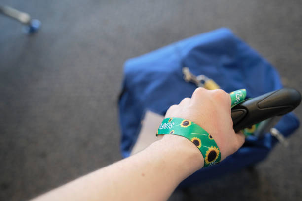 Hand of a person dragging a suitcase, wearing on the wrist a lanyard of sunflowers, symbol of people with invisible or hidden disabilities.