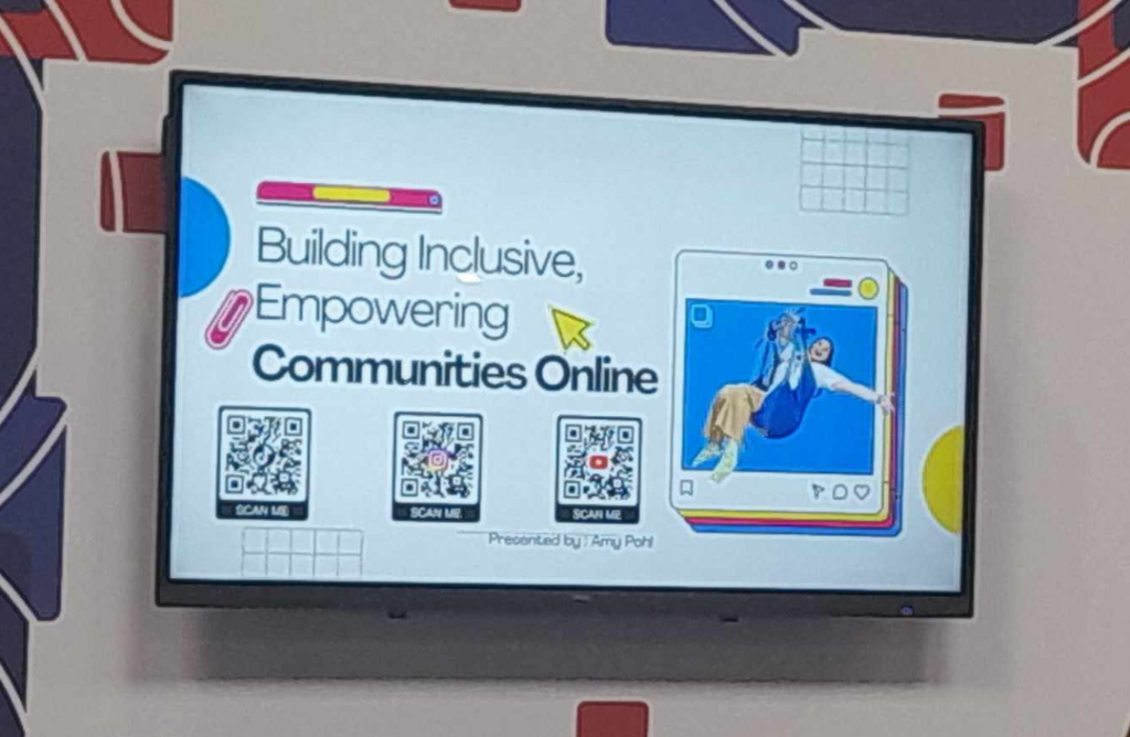 A white screen showing a presentation. The slide has the heading "Building Inclusive, Empowering Communities Online" with 3 QR codes underneath. To the right is a graphic of Amy Pohl smiling in a hoist.
