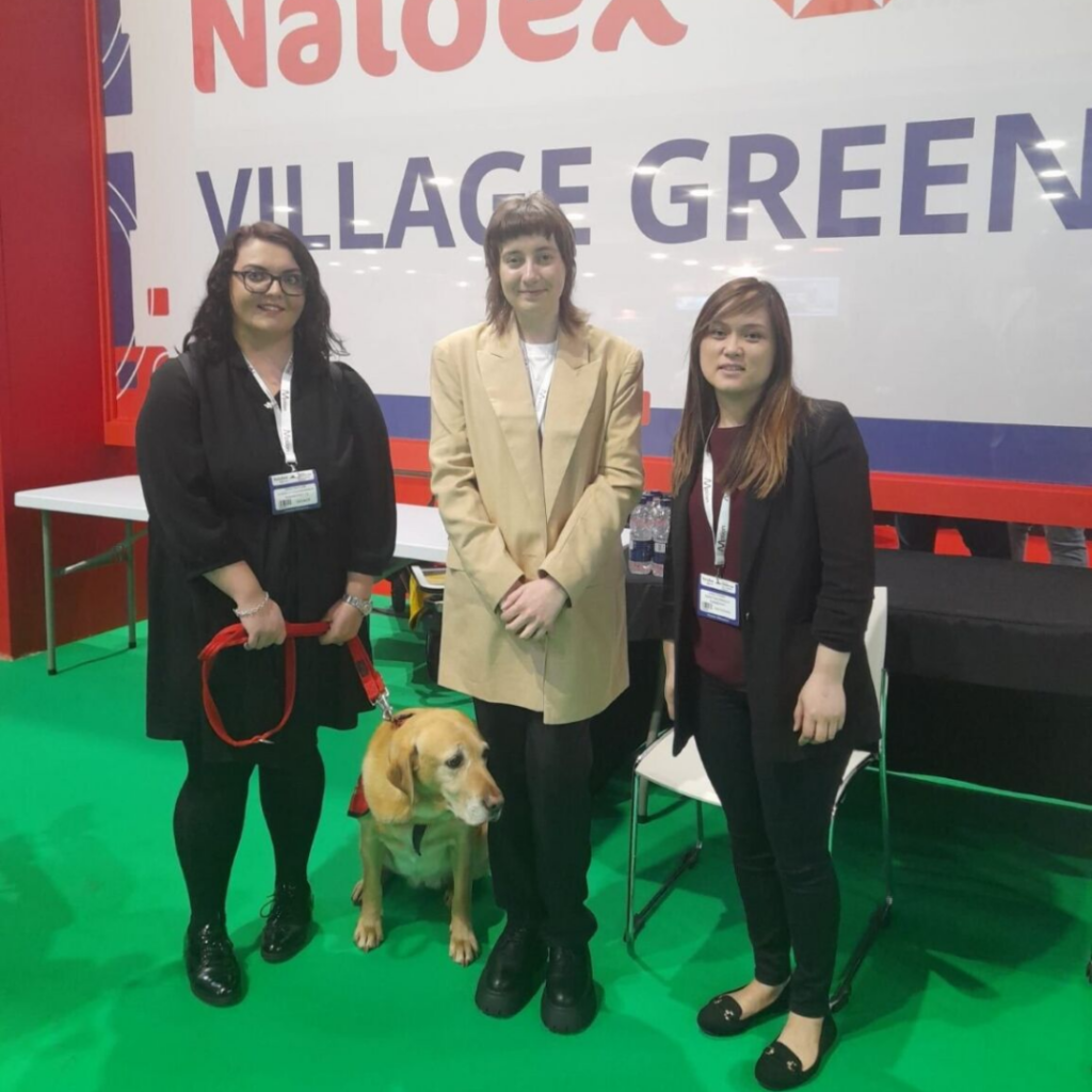 From left to right: Emma Partlow, a caucasian woman with dark hair and glasses, holding her assistance dog Luna on a red lead. Mary Senier, a caucasian woman with short brown hair and a long tan blazer. Linda Truong, a south east asian woman with long brown hair, a black suit and a purple jumper.