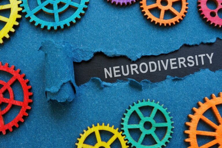The background is blue paper and this is ripped to reveal the word "neurodiversity" in white text on a black background. On top of the blue paper are colourful cogs.