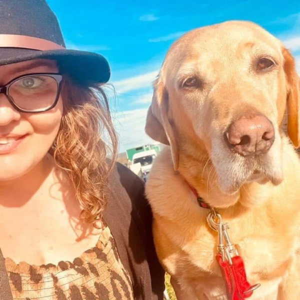 Emma with her assistance dog Luna under a bright blue sky with glowing sunlight.