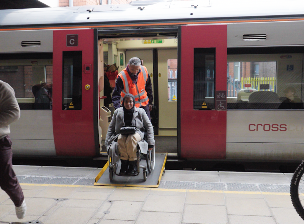 Umaymah, a Disabled wheelchair user, leaving a train using a ramp with support from station staff.