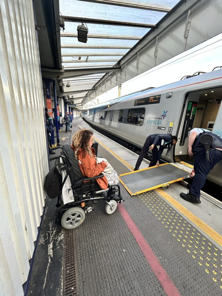 Carrie Ann Lightley waits on a train platform while station staff prepare a ramp for her to board the train.