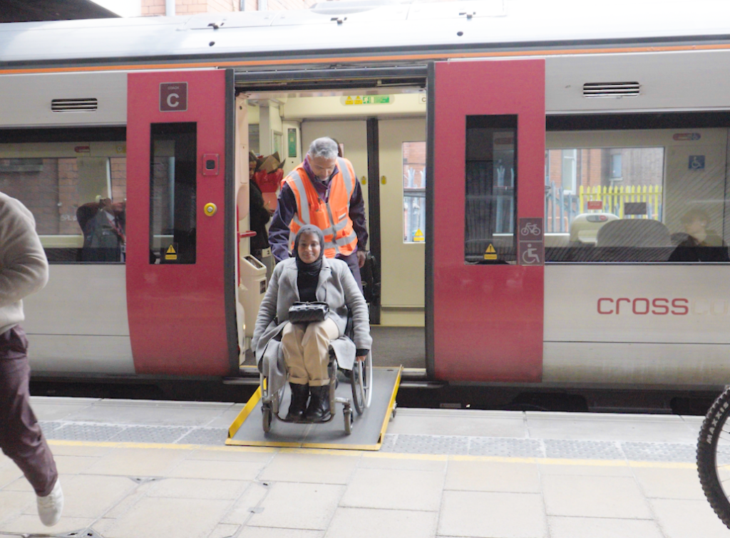A wheelchair user getting off the train using a ramp, with staff providing assistance