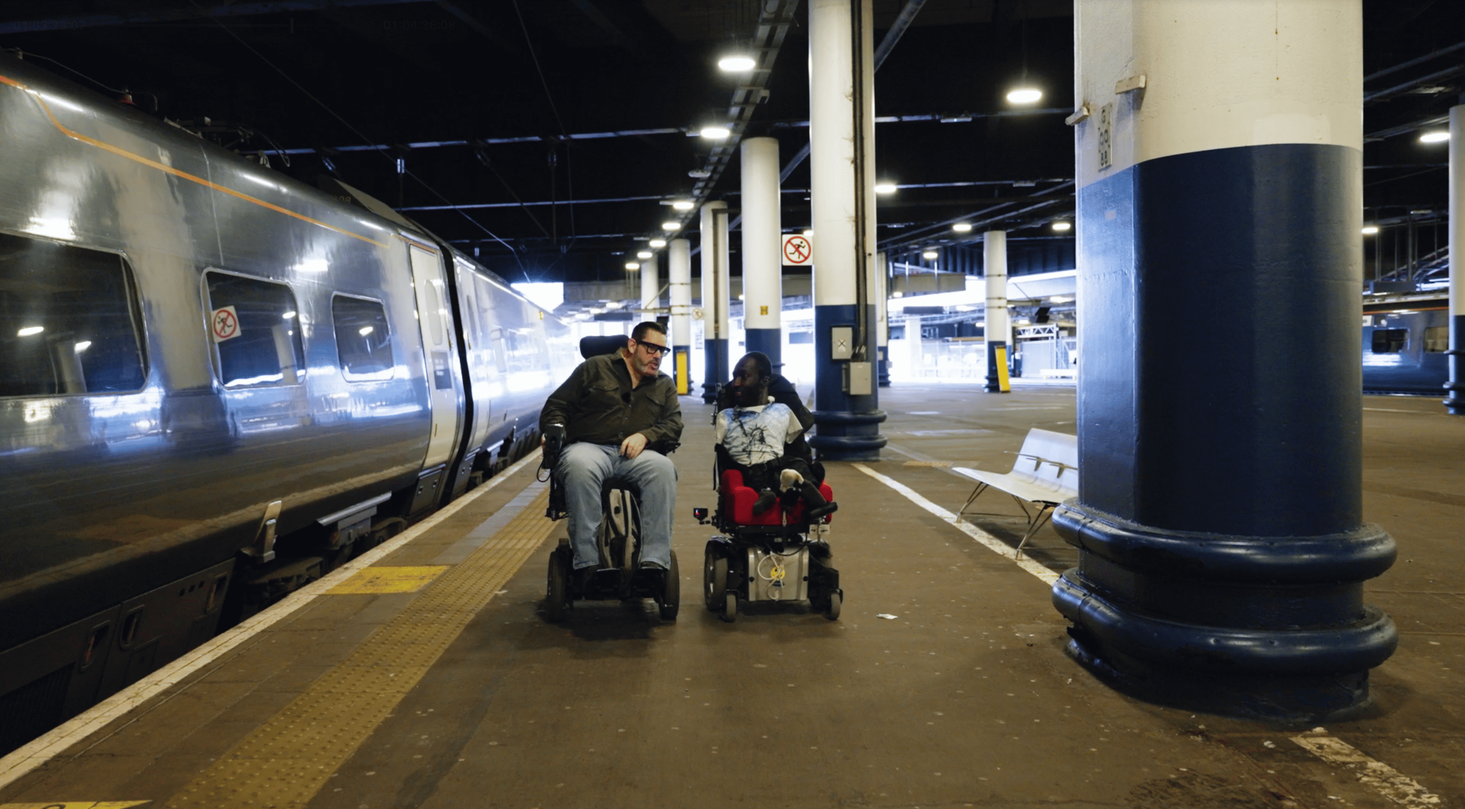 Two wheelchair users talking at the train station's platform.