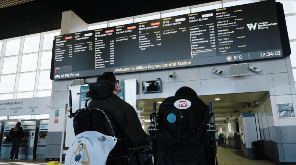 Two wheelchair users checking their journey details on the train information board