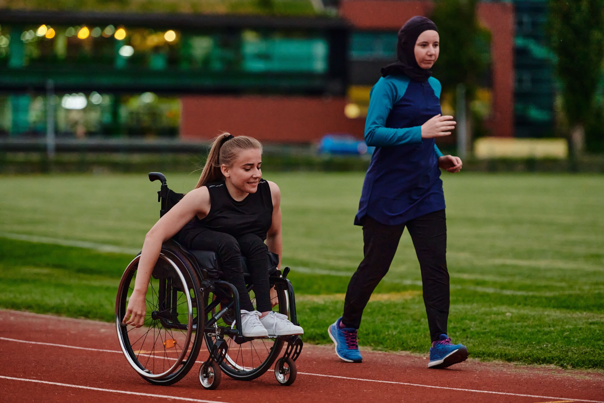 A Muslim woman wearing a burqa supports her friend who is a wheelchair user on a track