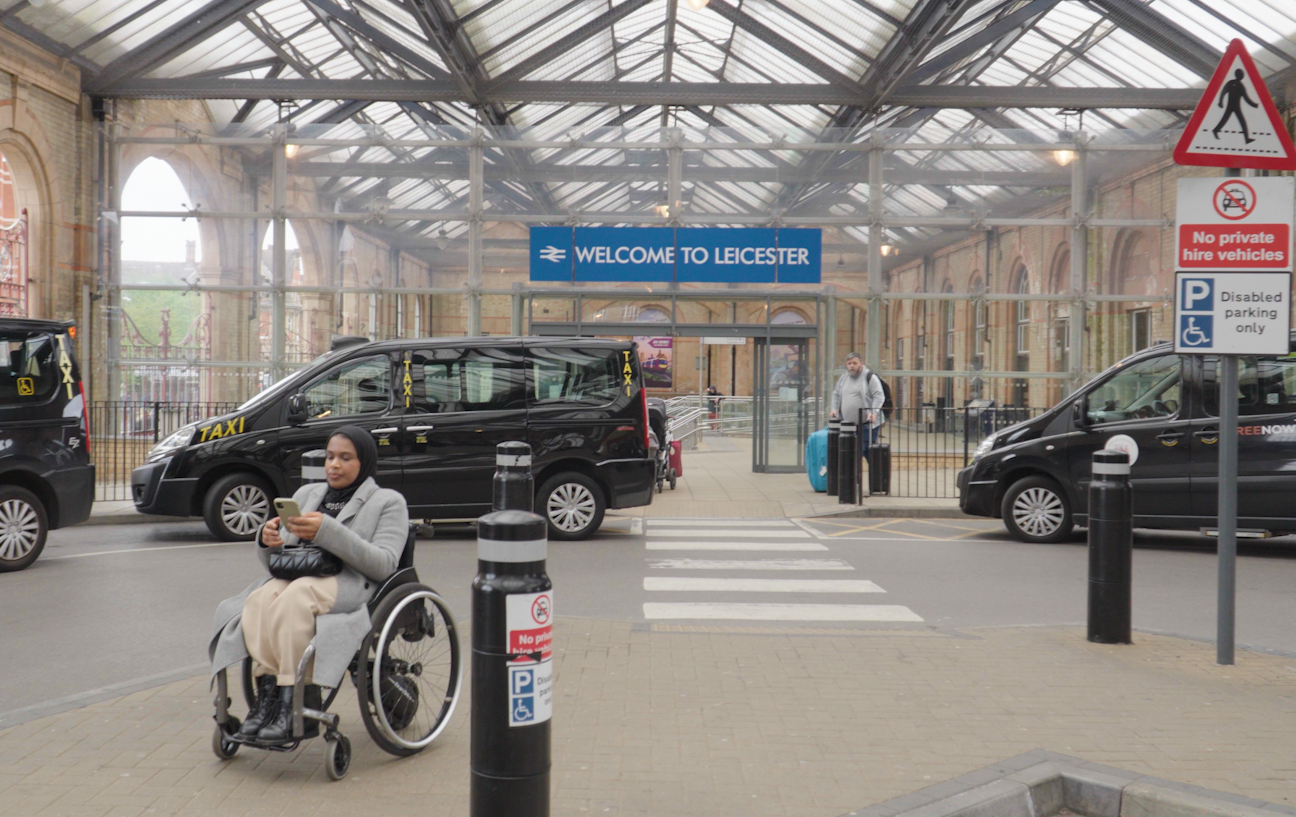 Umaymah, a wheelchair user, is looking at her phone while leaving the train station